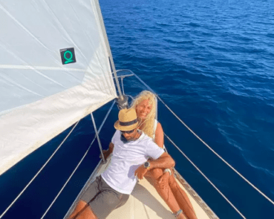 Una pareja se relaja en la cubierta de un velero bajo el cielo azul y el mar en calma de la Costa Brava, disfrutando de su tranquilo Paseo exclusivo en Velero en la Costa Brava. - ForTwo - Planes para parejas