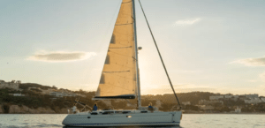 El exclusivo Paseo Velero en la Costa Brava se desliza sobre aguas tranquilas durante una serena puesta de sol, con las pintorescas colinas y edificios suavemente recortados en el fondo. - ForTwo - Planes para parejas