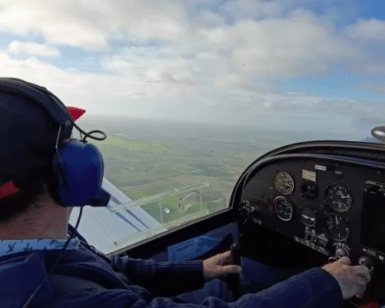 En la cabina de un pequeño avión, una persona disfruta de la emoción de ser Piloto por un Día en Córdoba, con unos auriculares y una gorra azules mientras vuela sobre el paisaje rural en un día claro. - ForTwo - Planes para parejas