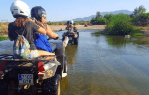 Los ciclistas del "Quad por el río Guadalhorce" recorren un arroyo de poca profundidad, con majestuosas montañas que proporcionan un impresionante telón de fondo que recuerda los paisajes escénicos cercanos al río. - ForTwo - Planes para parejas