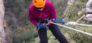 Alguien lleva puesto un casco y desciende con destreza por el acantilado empinado y herboso usando equipo avanzado, evocando la emocionante experiencia de Rápel en Cueva Mur. - ForTwo - Planes para parejas