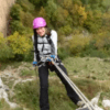Con un casco rosa, una persona sube hábilmente una pendiente rocosa con cuerdas, acercándose a la entrada de Cueva Mur para una aventura de Rápel en Cueva Mur. - ForTwo - Planes para parejas