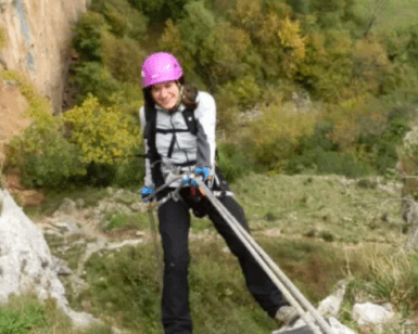 Con un casco rosa, una persona sube hábilmente una pendiente rocosa con cuerdas, acercándose a la entrada de Cueva Mur para una aventura de Rápel en Cueva Mur. - ForTwo - Planes para parejas