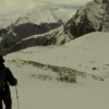 Dos personas esquían por una montaña nevada con nubes y picos lejanos, que recuerdan a los majestuosos Picos de Europa, similar a la experiencia que ofrecen Raquetas de Nieve en Picos de Europa. - ForTwo - Planes para parejas