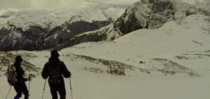 Dos personas esquían por una montaña nevada con nubes y picos lejanos, que recuerdan a los majestuosos Picos de Europa, similar a la experiencia que ofrecen Raquetas de Nieve en Picos de Europa. - ForTwo - Planes para parejas