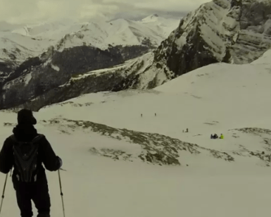 Dos personas esquían por una montaña nevada con nubes y picos lejanos, que recuerdan a los majestuosos Picos de Europa, similar a la experiencia que ofrecen Raquetas de Nieve en Picos de Europa. - ForTwo - Planes para parejas