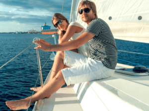 Una pareja disfruta de su recorrido romántico en catamarán, con gafas de sol y con el agua azul clara de fondo. - ForTwo - Planes para parejas