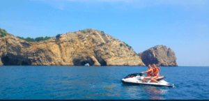 Una emocionante aventura se desarrolla en una Ruta en Moto de Agua por las Islas Medas, mientras dos motociclistas se deslizan por el vibrante océano, con los majestuosos acantilados rocosos de las Islas Medas como telón de fondo impresionante. - ForTwo - Planes para parejas