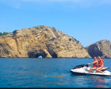 Una emocionante aventura se desarrolla en una Ruta en Moto de Agua por las Islas Medas, mientras dos motociclistas se deslizan por el vibrante océano, con los majestuosos acantilados rocosos de las Islas Medas como telón de fondo impresionante. - ForTwo - Planes para parejas