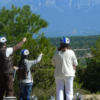 Cuatro aventureros con casco, apuntando a montañas distantes y rodeados de exuberante vegetación, se embarcan en una emocionante "Ruta en Segway por Asque" a través del pintoresco paisaje. - ForTwo - Planes para parejas