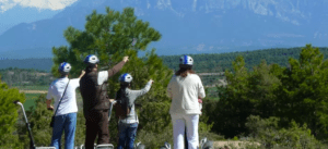 Cuatro aventureros con casco, apuntando a montañas distantes y rodeados de exuberante vegetación, se embarcan en una emocionante "Ruta en Segway por Asque" a través del pintoresco paisaje. - ForTwo - Planes para parejas