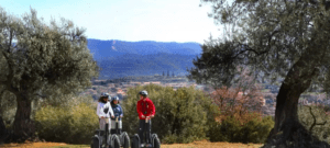 Tres personas se embarcan en una Ruta en Segway por Asque, navegando entre olivos con el pintoresco pueblo de Asque y majestuosas montañas como telón de fondo. - ForTwo - Planes para parejas