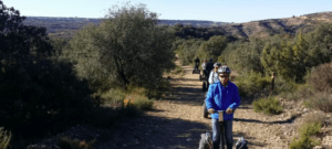 Los participantes de la "Ruta en Segway por Asque" se deslizan por un sendero de tierra, rodeado de frondosos árboles, navegando por el paisaje montañoso. - ForTwo - Planes para parejas