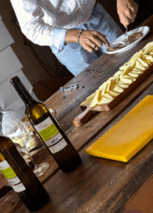 Con destreza, se prepara comida con queso y vino en una mesa de madera, abrazando el "Sabor y tradición en los Valles Pasiegos", donde cada bocado celebra el sabor. - ForTwo - Planes para parejas