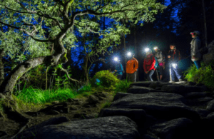Los excursionistas se embarcan en una aventura de Senderismo Nocturno en Menorca, recorriendo un camino rocoso y utilizando linternas frontales para iluminar la encantadora noche. - ForTwo - Planes para parejas