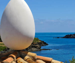 Encaramada en un tejado, una gran escultura de piedra con forma de huevo domina la escarpada costa y el mar infinito, reflejando el encanto de Portlligat. Los visitantes experimentan la "Visita la Casa de Dalí en Portlligat" con su surrealista encanto paisajístico. - ForTwo - Planes para parejas