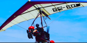 Una persona que pilota la vibrante Vuela el Guadalquivir con Ala Delta Motorizada de color rojo se eleva elegantemente contra el cielo azul claro, encarnando la emoción de volar. - ForTwo - Planes para parejas
