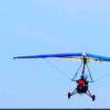 Un ultraligero rojo y azul llamado Vuela el Guadalquivir con Ala Delta Motorizada se desliza por el cielo azul claro, capturando la esencia de volar sobre la serena belleza del Guadalquivir. - ForTwo - Planes para parejas