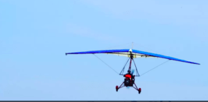 Un ultraligero rojo y azul llamado Vuela el Guadalquivir con Ala Delta Motorizada se desliza por el cielo azul claro, capturando la esencia de volar sobre la serena belleza del Guadalquivir. - ForTwo - Planes para parejas