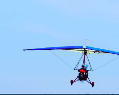 Un ultraligero rojo y azul llamado Vuela el Guadalquivir con Ala Delta Motorizada se desliza por el cielo azul claro, capturando la esencia de volar sobre la serena belleza del Guadalquivir. - ForTwo - Planes para parejas