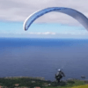 Surcando los cielos, alguien realiza un parapente con "Vuela en Pareja sobre la Costa Cántabra", rodeado de una impresionante vista al mar y un cielo nublado de fondo. - ForTwo - Planes para parejas
