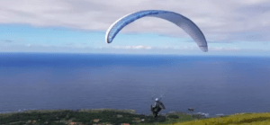 Surcando los cielos, alguien realiza un parapente con "Vuela en Pareja sobre la Costa Cántabra", rodeado de una impresionante vista al mar y un cielo nublado de fondo. - ForTwo - Planes para parejas