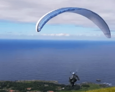 Surcando los cielos, alguien realiza un parapente con "Vuela en Pareja sobre la Costa Cántabra", rodeado de una impresionante vista al mar y un cielo nublado de fondo. - ForTwo - Planes para parejas