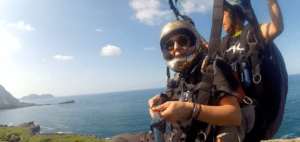 Dos personas volando en parapente sobre la impresionante Costa Cántabra, frente a un sereno cielo azul y un vasto océano, personifican la esencia de "Vuela en Pareja sobre la Costa Cántabra. - ForTwo - Planes para parejas
