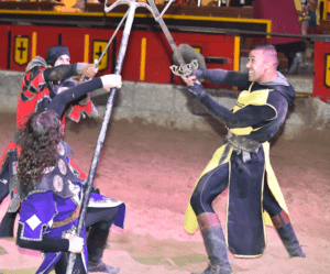 En el corazón de Tenerife, tres artistas con armadura medieval deslumbran al público con Aventura Medieval en Tenerife, participando en una emocionante batalla escenificada con armas en una gran arena. - ForTwo - Planes para parejas