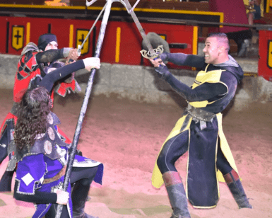 En el corazón de Tenerife, tres artistas con armadura medieval deslumbran al público con Aventura Medieval en Tenerife, participando en una emocionante batalla escenificada con armas en una gran arena. - ForTwo - Planes para parejas