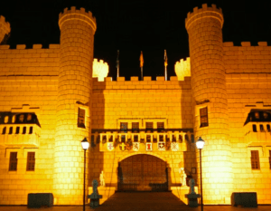 Un castillo brillantemente iluminado en Tenerife, Aventura Medieval en Tenerife, se alza majestuoso por la noche con dos torres redondas y una gran entrada central. - ForTwo - Planes para parejas