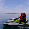 Dos personas con chalecos salvavidas navegan en una Aventura en Moto de Agua en Valencia por las tranquilas aguas bajo un cielo azul con nubes ligeras, abrazando el espíritu de aventura. - ForTwo - Planes para parejas