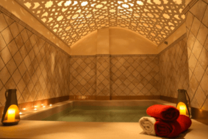 Los Baños Árabes en Menorca ofrecen una lujosa experiencia de spa con una piscina iluminada con velas, un techo ornamentado y toallas rojas y blancas cuidadosamente apiladas que reflejan el encanto de Menorca. - ForTwo - Planes para parejas