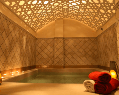 Los Baños Árabes en Menorca ofrecen una lujosa experiencia de spa con una piscina iluminada con velas, un techo ornamentado y toallas rojas y blancas cuidadosamente apiladas que reflejan el encanto de Menorca. - ForTwo - Planes para parejas