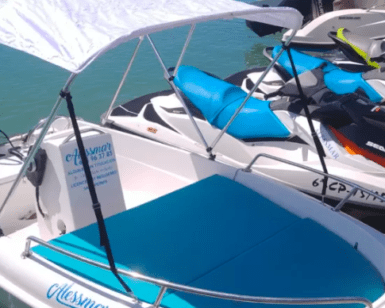 Un barco sin licencia en Alcossebre, con casco blanco, toldo y asientos azules, está atracado junto a motos de agua en las aguas turquesas y disponible para alquilar. - ForTwo - Planes para parejas