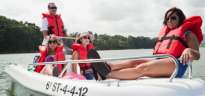 Cuatro personas con chalecos salvavidas navegan pacíficamente en una pequeña embarcación a través de un exuberante lago verde, capturando el encanto de Santander y la libertad de un Barco sin licencia en Santander. - ForTwo - Planes para parejas