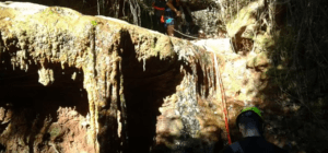 Dos aventureros, apasionados del barranquismo en la Sierra de Cardeña y Montoro, hacen rappel con destreza por una cascada rocosa en el frondoso bosque. - ForTwo - Planes para parejas