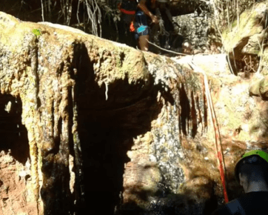 Dos aventureros, apasionados del barranquismo en la Sierra de Cardeña y Montoro, hacen rappel con destreza por una cascada rocosa en el frondoso bosque. - ForTwo - Planes para parejas