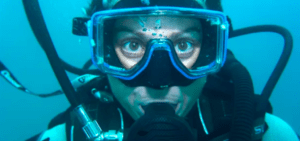 Un buceador sumergido en Alcocéber, equipado con máscara y equipo de respiración, con los ojos bien abiertos en medio de las aguas azules: una experiencia impresionante de Bautismo de Buceo en Alcocéber. - ForTwo - Planes para parejas