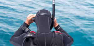 Un buceador con traje de neopreno negro, listo para un Bautismo de Buceo en Alcocéber, ajusta su máscara mientras admira la hermosa costa. - ForTwo - Planes para parejas