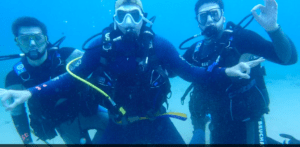 Tres buceadores bajo el agua en Tossa de Mar, con trajes de neopreno y máscaras negras, hacen un gesto a la cámara durante su Bautismo de Buceo en Tossa de Mar. - ForTwo - Planes para parejas