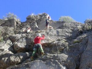 Bajo el claro cielo azul de Valencia, tres escaladores ascienden por un escarpado acantilado, asegurados con cuerdas. El Bautismo de escalada en Valencia: ¡una experiencia llena de desafío y conexión! promete una aventura inolvidable para todos los amantes de las emociones fuertes. - ForTwo - Planes para parejas