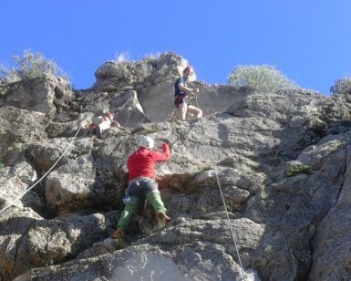 Bajo el claro cielo azul de Valencia, tres escaladores ascienden por un escarpado acantilado, asegurados con cuerdas. El Bautismo de escalada en Valencia: ¡una experiencia llena de desafío y conexión! promete una aventura inolvidable para todos los amantes de las emociones fuertes. - ForTwo - Planes para parejas