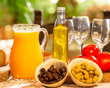 Un brunch vibrante se desarrolla con naranjas, tomates de Sóller, aceitunas, degustación de aceite de oliva y copas de vino dispuestas artísticamente como parte de la experiencia "Cata de Aceite de Oliva y Brunch en Sóller". - ForTwo - Planes para parejas