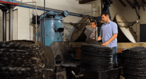 En un molino industrial de Sóller, dos expertos manejan pilas de aceitunas entre grandes máquinas y platos de prensa para elaborar el producto premium, Cata de Aceite de Oliva y Brunch en Sóller. - ForTwo - Planes para parejas