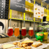 En el mostrador, junto a una rana verde, se encuentran una selección de cervezas ácidas y una tabla de quesos. Detrás, un menú presenta la experiencia "Cata de Cervezas Artesanas en Valencia". - ForTwo - Planes para parejas