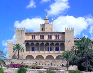 La Catedral de Mallorca y Palacio Real, una fortaleza histórica con arcos, torres y jardines bajo un cielo azul, está elegantemente situada junto al impresionante Palacio Real de Palma de Mallorca. - ForTwo - Planes para parejas