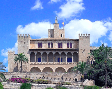 La Catedral de Mallorca y Palacio Real, una fortaleza histórica con arcos, torres y jardines bajo un cielo azul, está elegantemente situada junto al impresionante Palacio Real de Palma de Mallorca. - ForTwo - Planes para parejas