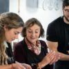 Tres personas con delantales cocinan juntas alegremente, capturando el vibrante espíritu de Valencia mientras disfrutan de una "Clase de cocina española en Valencia: tapas y vinos". - ForTwo - Planes para parejas
