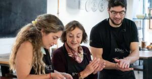 Tres personas con delantales cocinan juntas alegremente, capturando el vibrante espíritu de Valencia mientras disfrutan de una "Clase de cocina española en Valencia: tapas y vinos". - ForTwo - Planes para parejas